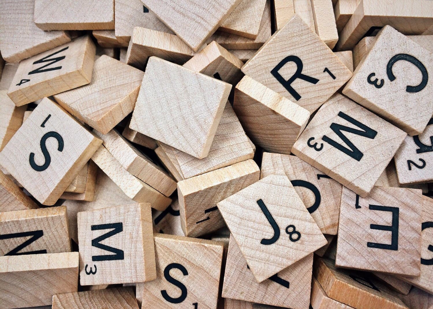 Houten Scrabble letters verstrooid, symboliserend de complexiteit en schoonheid van communicatie, relevant voor de zorg voor mensen met communicatie- en gehoorproblemen.